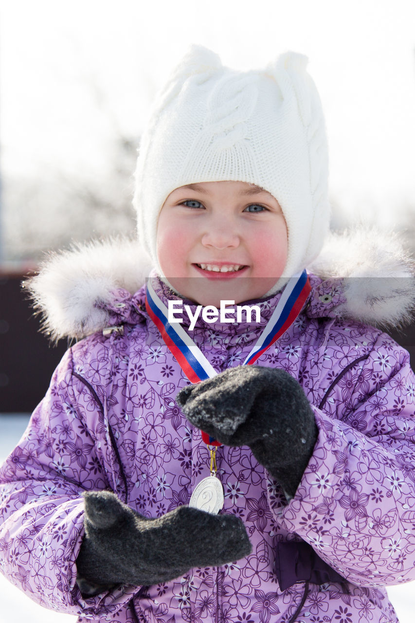 Portrait of cute girl holding medal while standing outdoors during winter