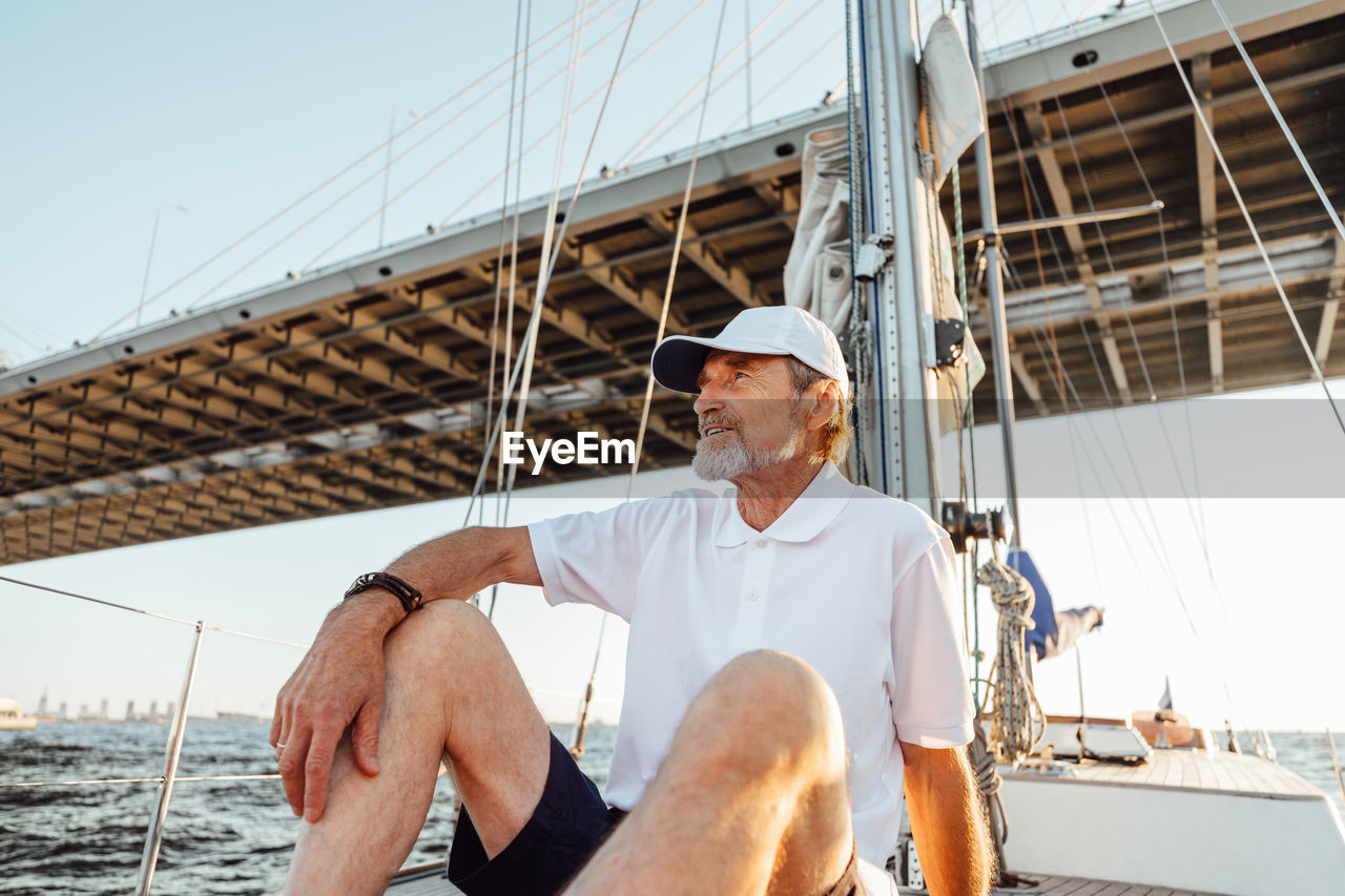 Senior man sitting on sailboat in sea against sky