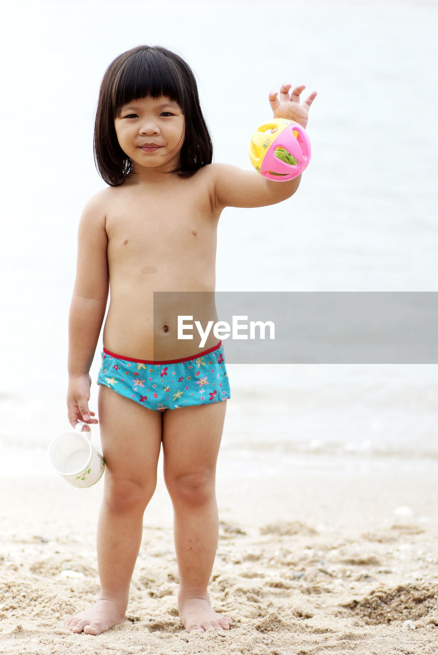 Portrait of shirtless girl holding toy while standing at beach