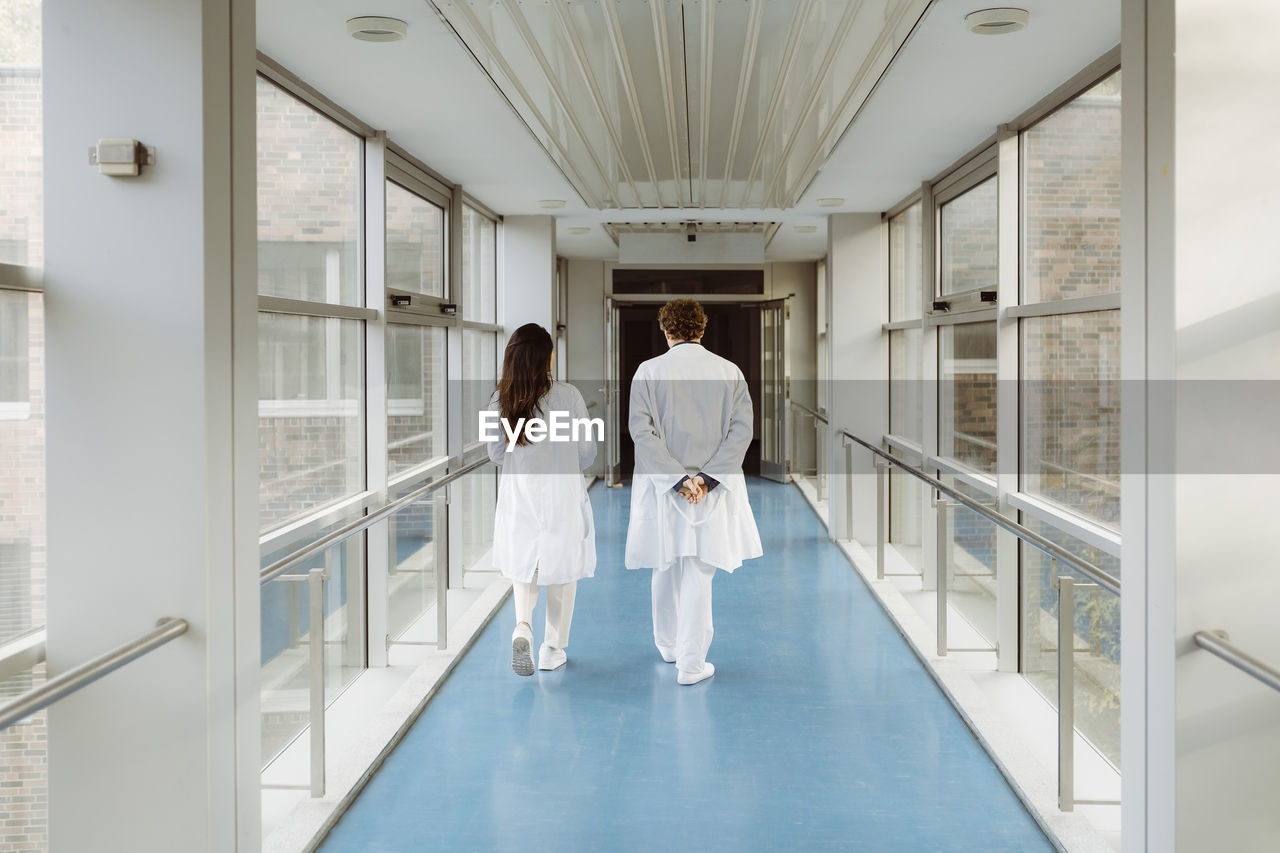 Full length rear view of male and female doctors discussing while walking together in hospital corridor