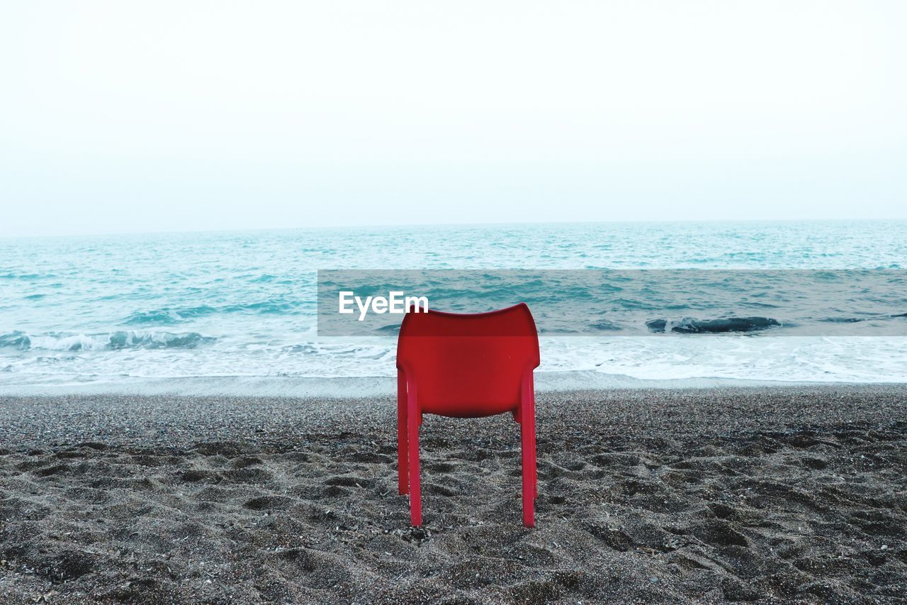 Red chair on beach against clear sky