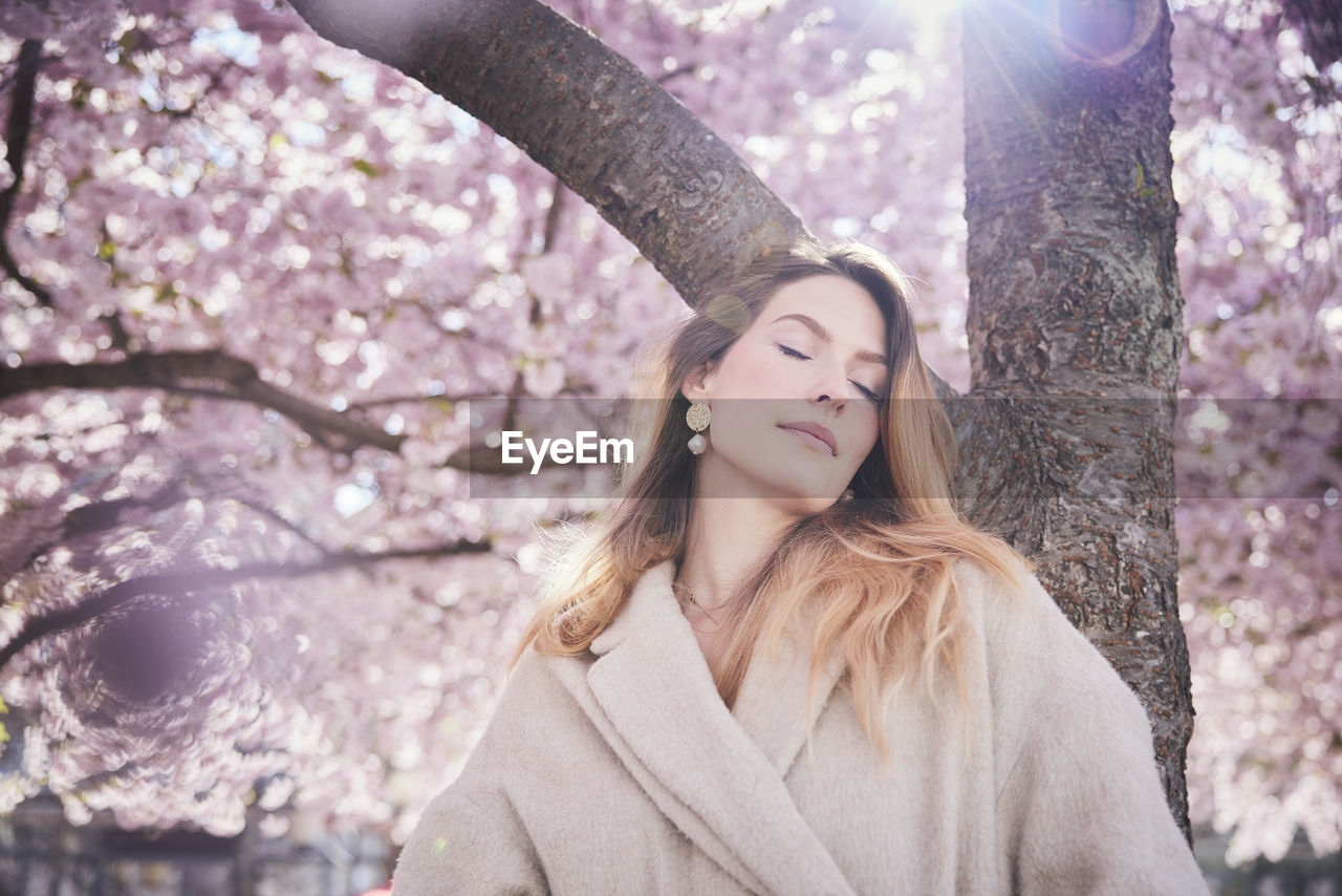 Young woman standing under cherry blossom