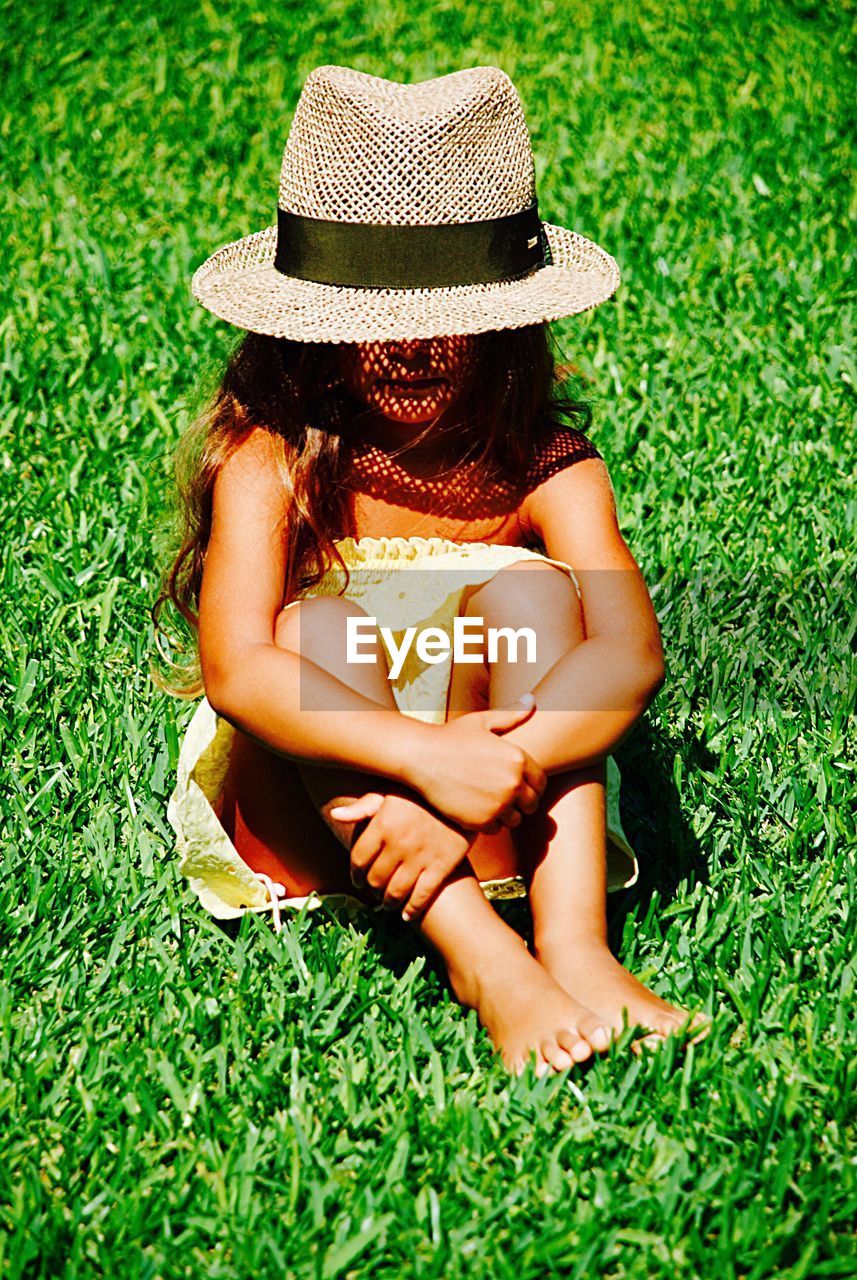 Full length of girl wearing hat sitting on grassy field