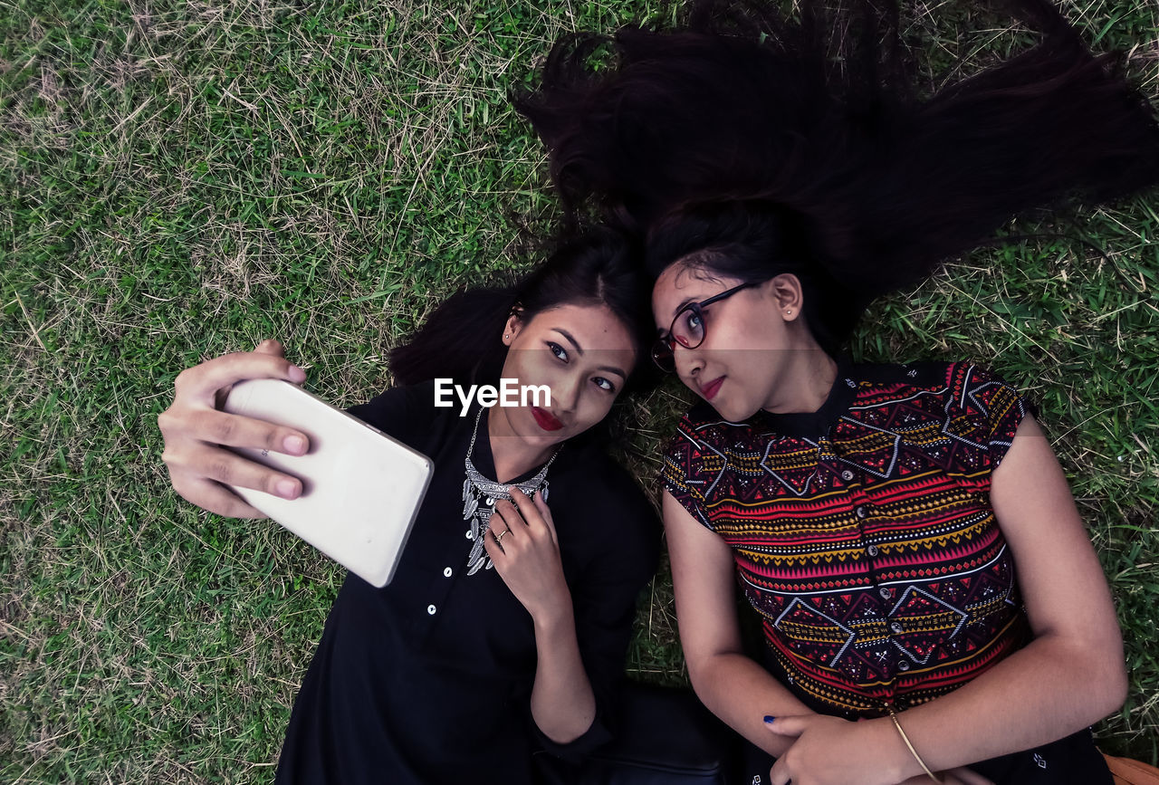 High angle view of female friends taking selfie while lying on grass