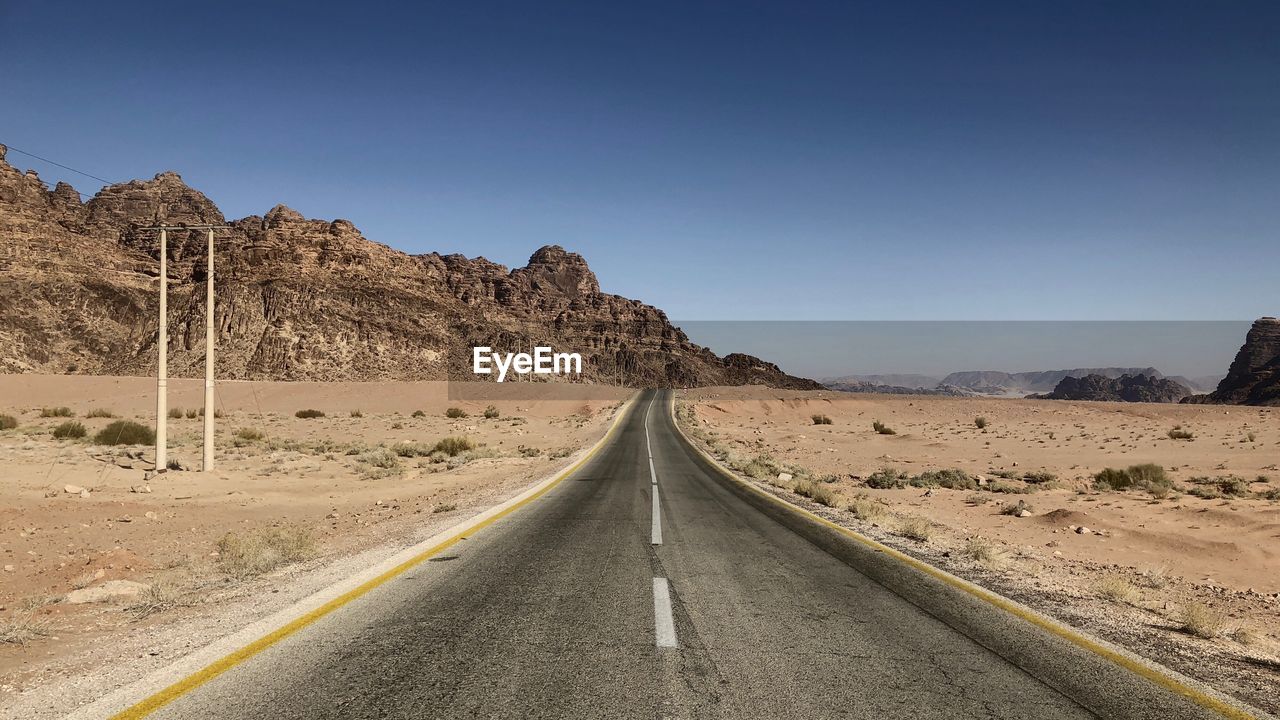 Road leading towards mountains against clear sky