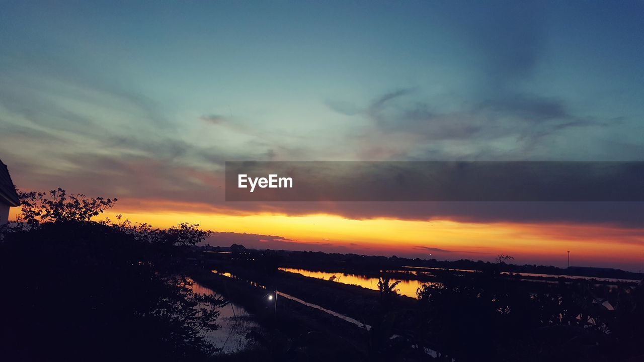 SCENIC VIEW OF DRAMATIC SKY OVER SILHOUETTE TREES AGAINST SUNSET