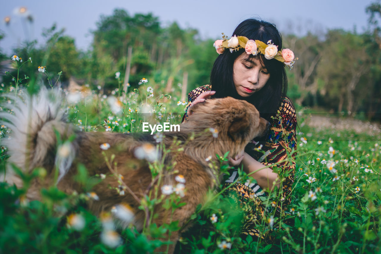 Woman wearing flowers while sitting with dog on field 