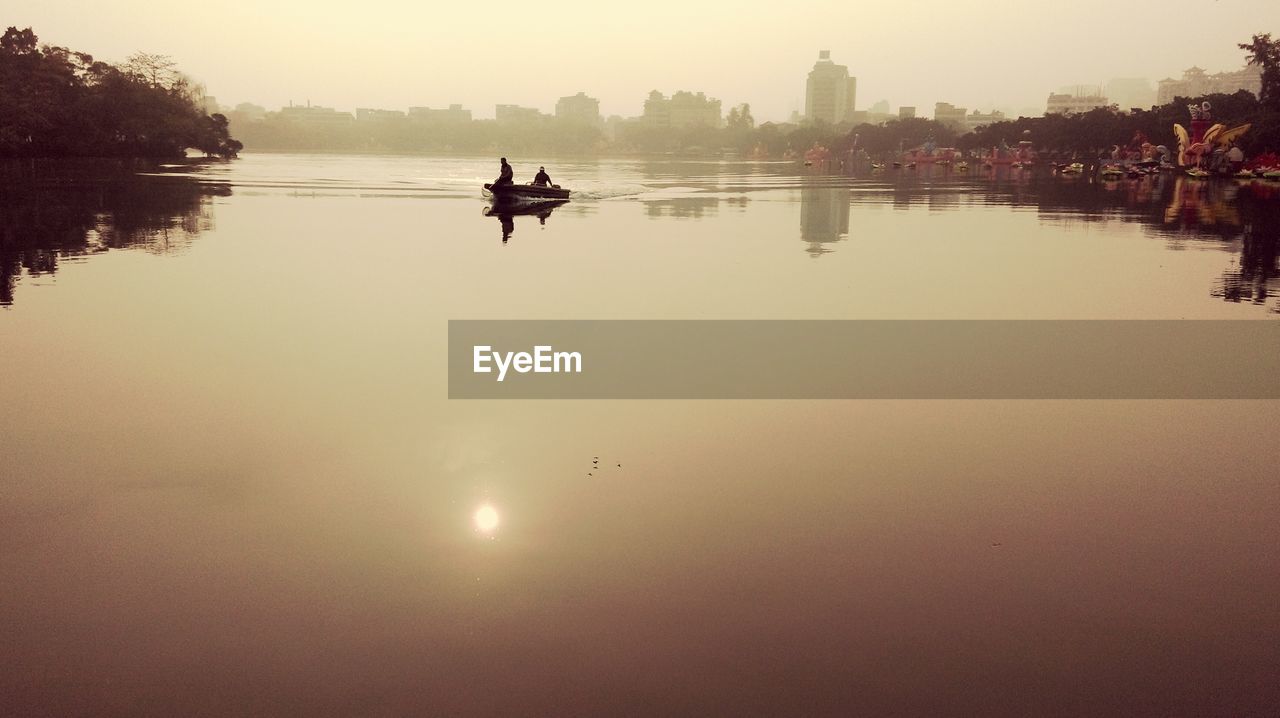 Silhouette men on boat sailing in river at sunrise