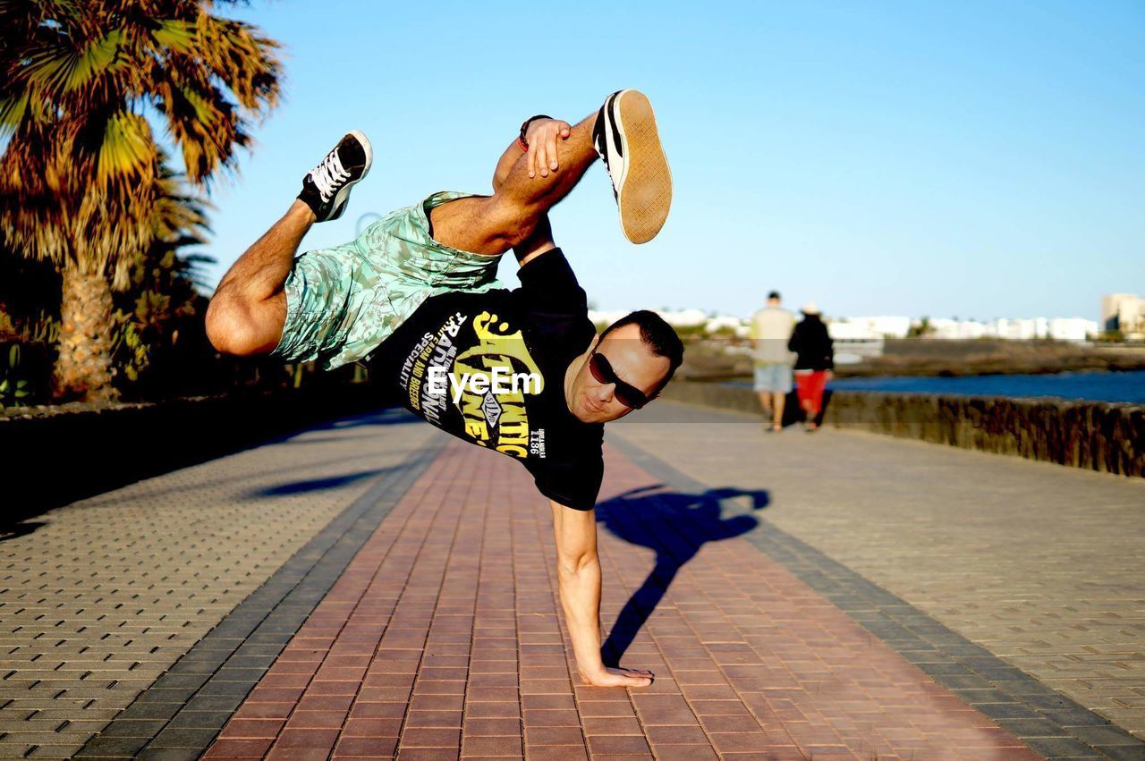 Young man practicing handstand on footpath