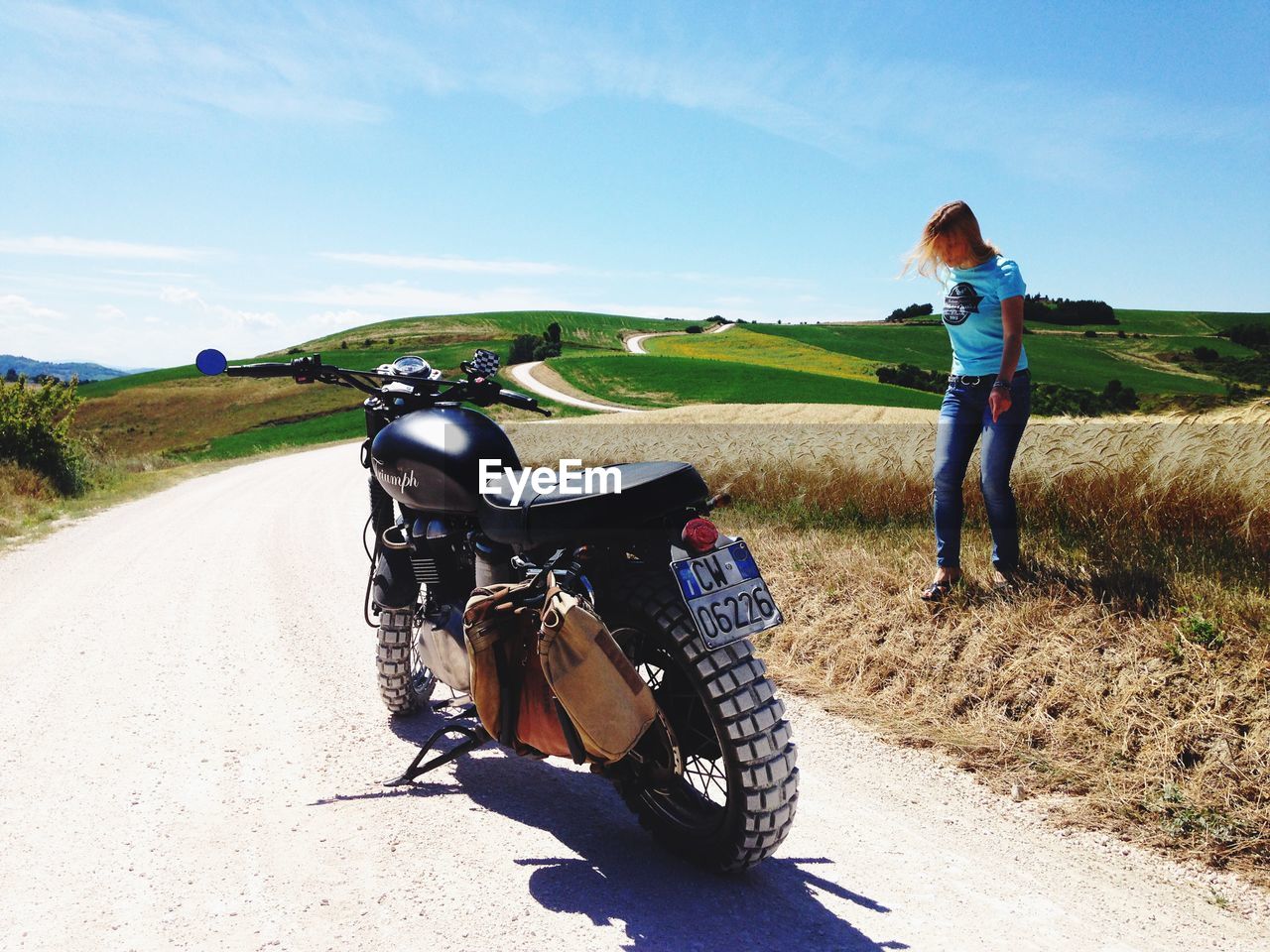 REAR VIEW OF WOMAN RIDING BICYCLE ON ROAD AGAINST SKY