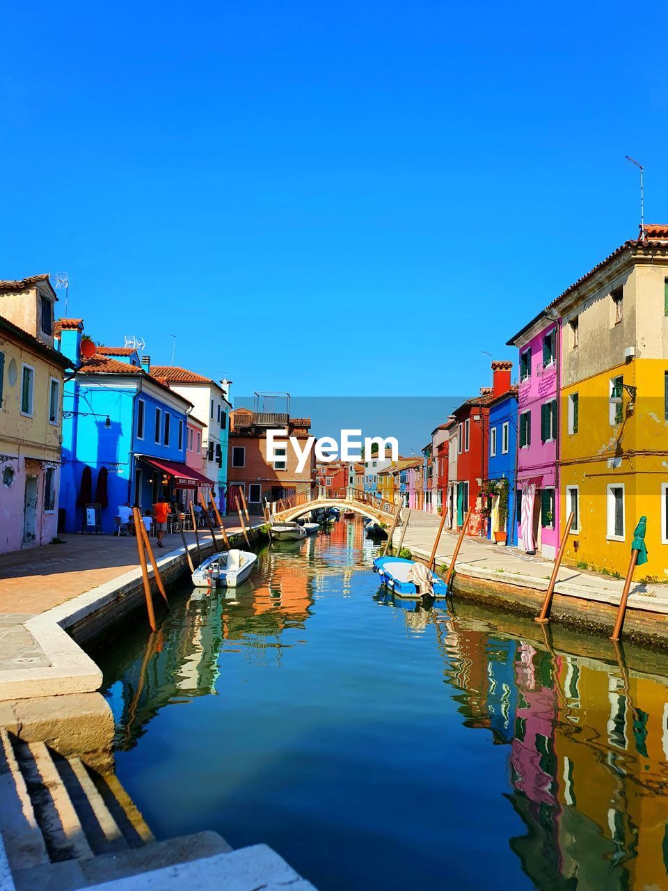 Canal amidst houses against clear blue sky