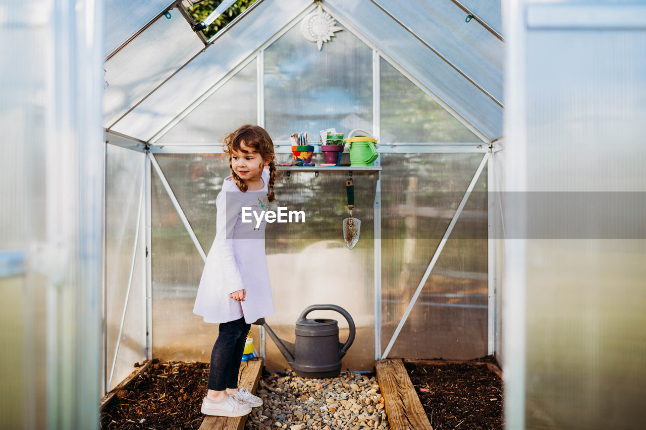 Young girl standing on plant bed in greenhouse in spring