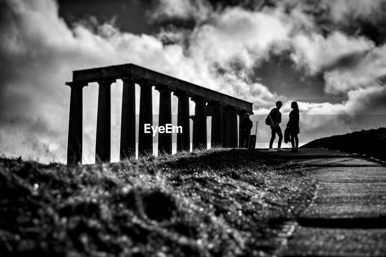 MEN WALKING ON GRASS AGAINST SKY