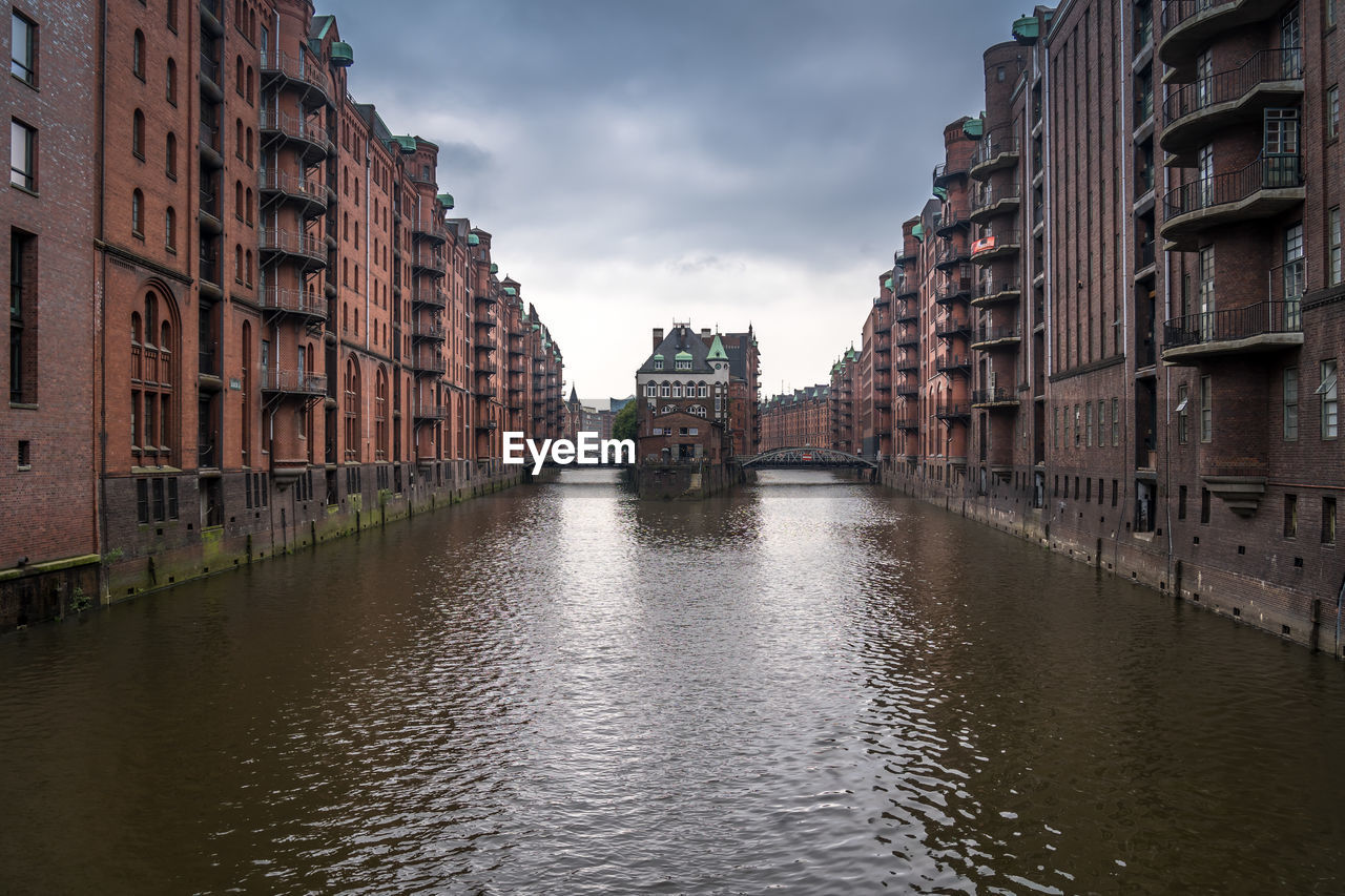 Canal amidst buildings in city against sky