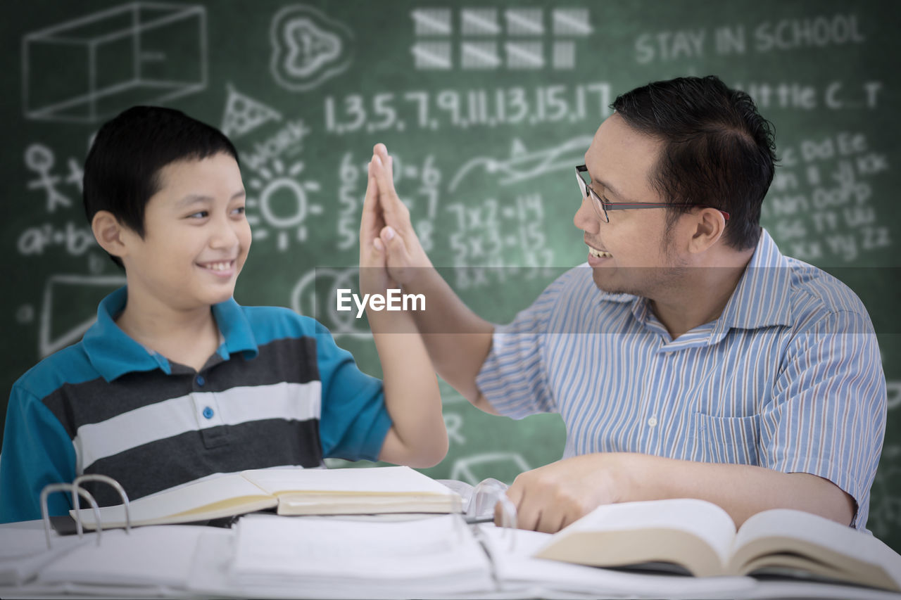 Boy with teacher at table against blackboard