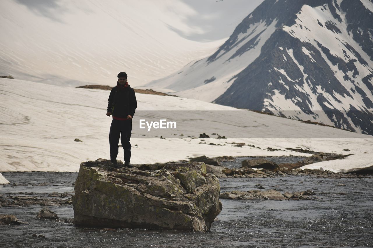 Full length of man standing on rock against snowcapped mountains