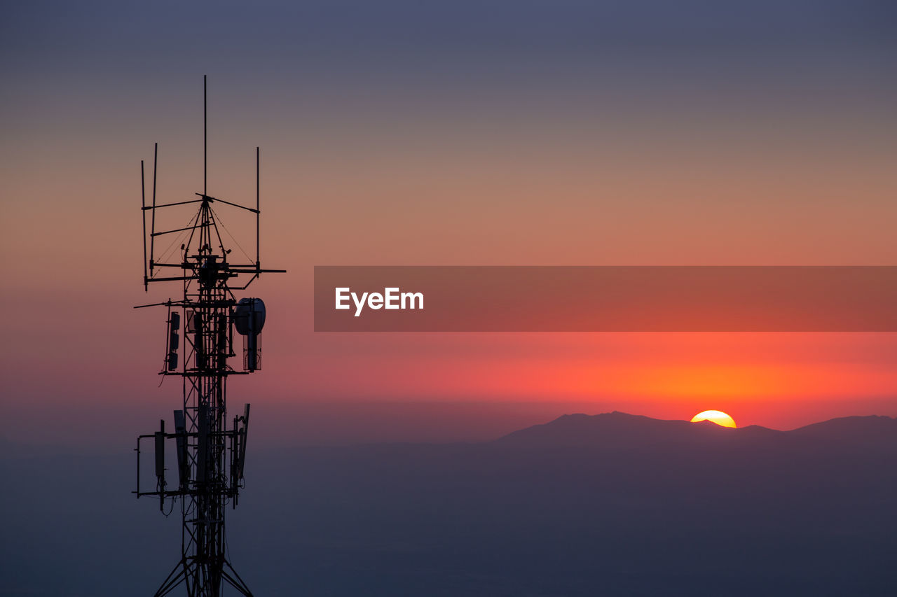 Silhouette of communications tower against orange sky