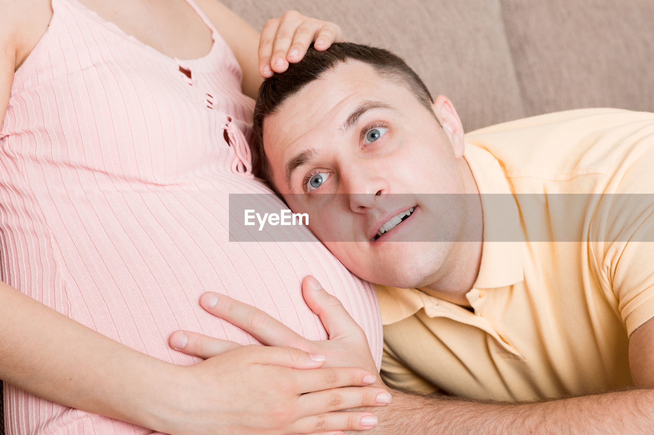 Man is listening to his beautiful pregnant wife tummy and smiling at the home.