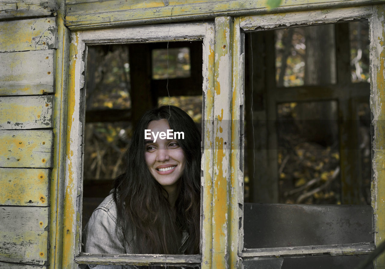 Portrait of smiling young woman against window