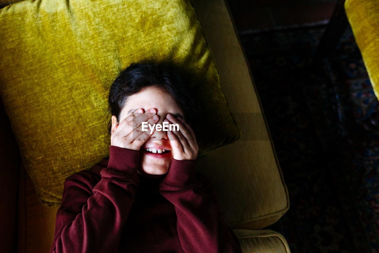 Upper view on child covering eyes laying on yellow sofa