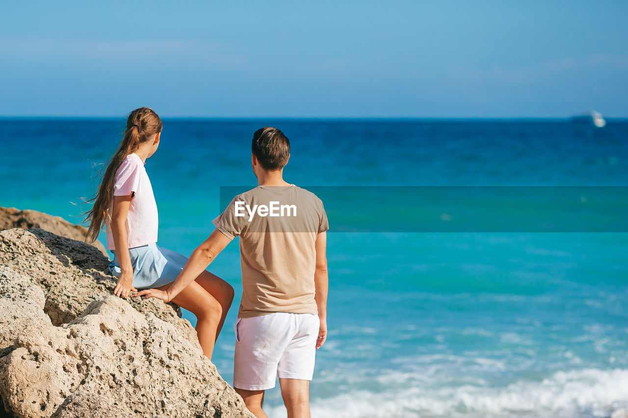 side view of woman sitting on rock at beach