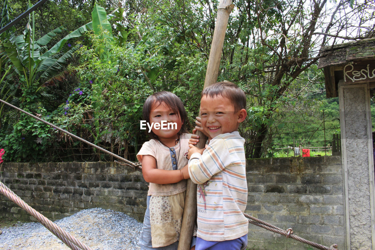 PORTRAIT OF SMILING BOY STANDING AGAINST TREE