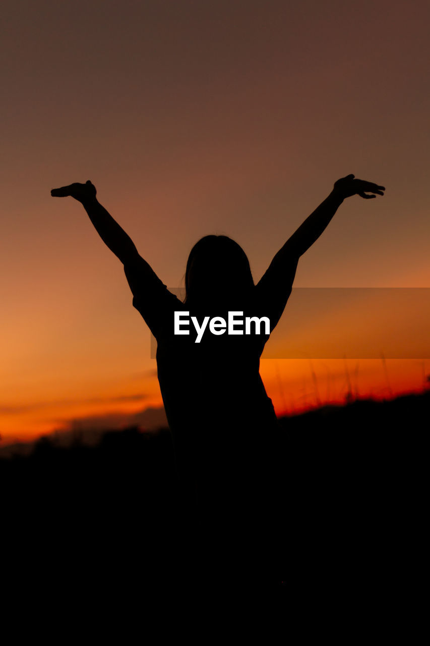 silhouette man with arms raised standing against clear sky during sunset