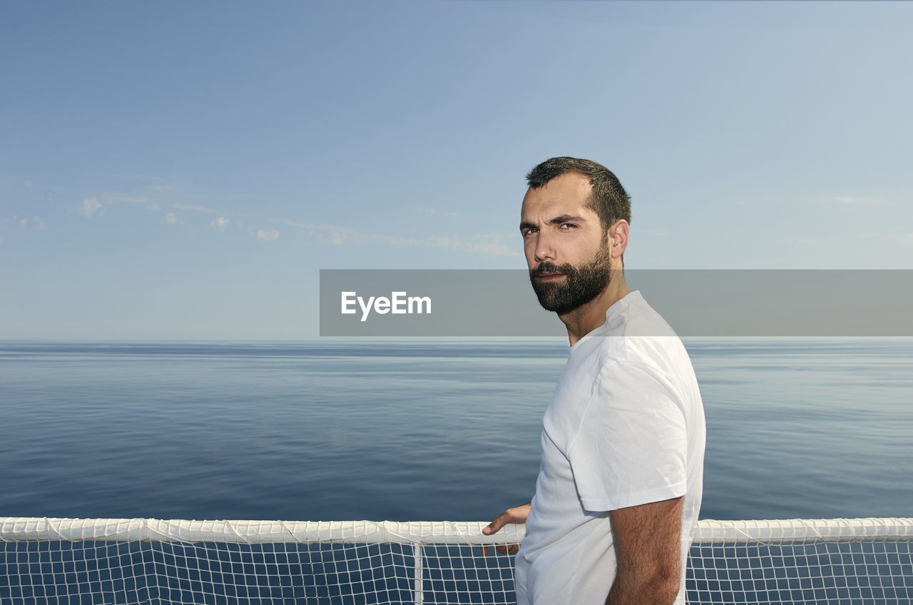 Portrait of serious man standing on cruise ship against sea