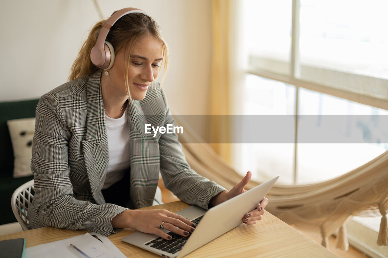 Young woman working at home with laptop on desk and headphones.  notebook for working. 