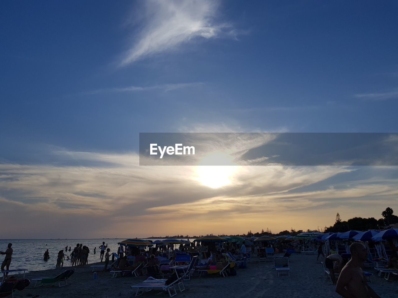 People at beach against sky during sunset