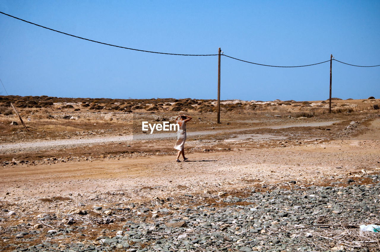 Full length of woman walking on sand against clear sky