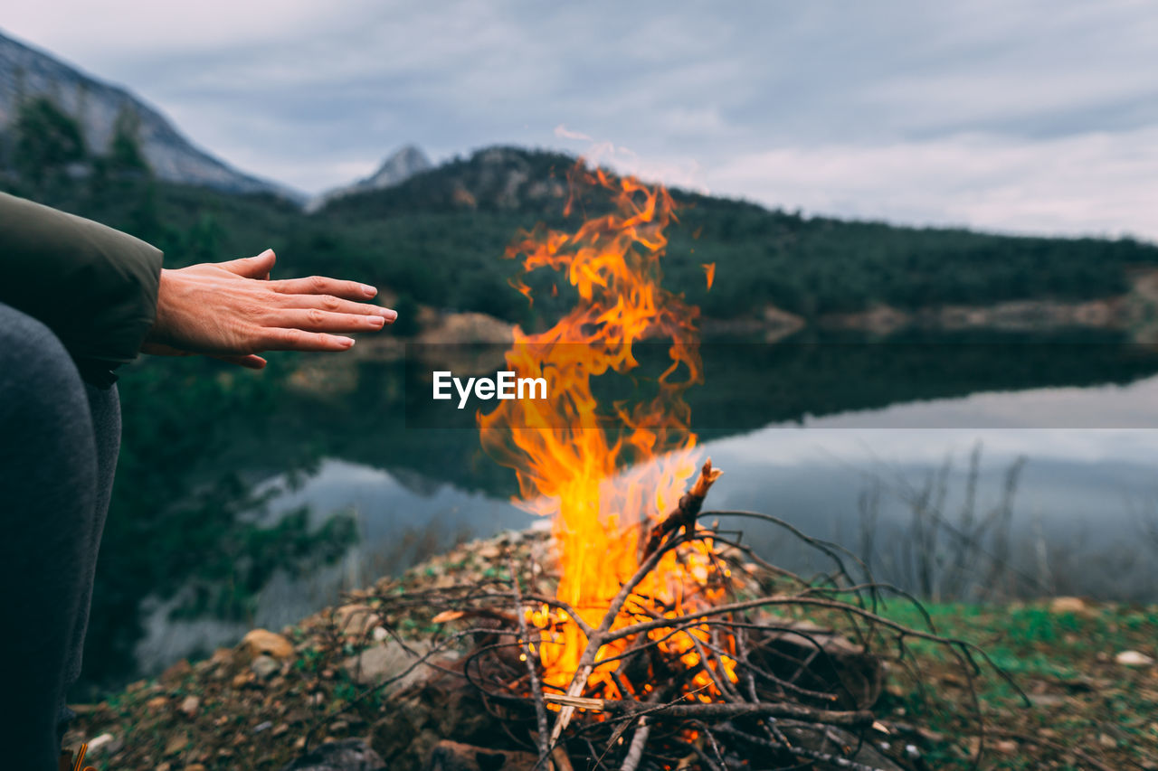 Midsection of woman by fire and lake against sky