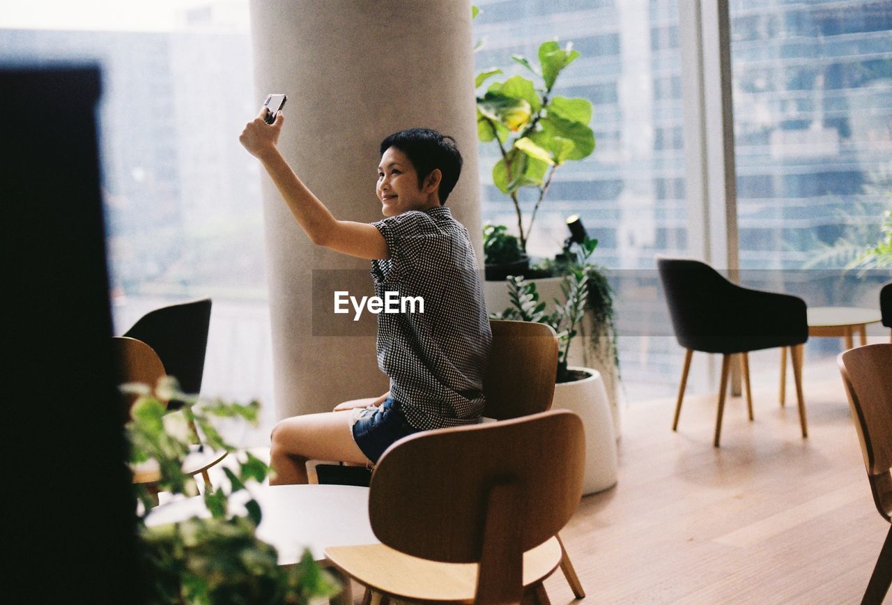 Woman taking selfie through mobile phone against window