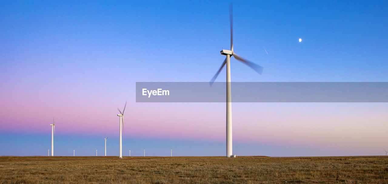 Wind turbines in field against blue sky at dusk