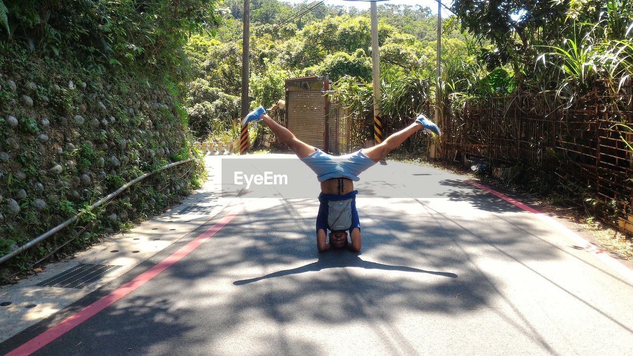 Full length of man performing headstand with legs apart on street