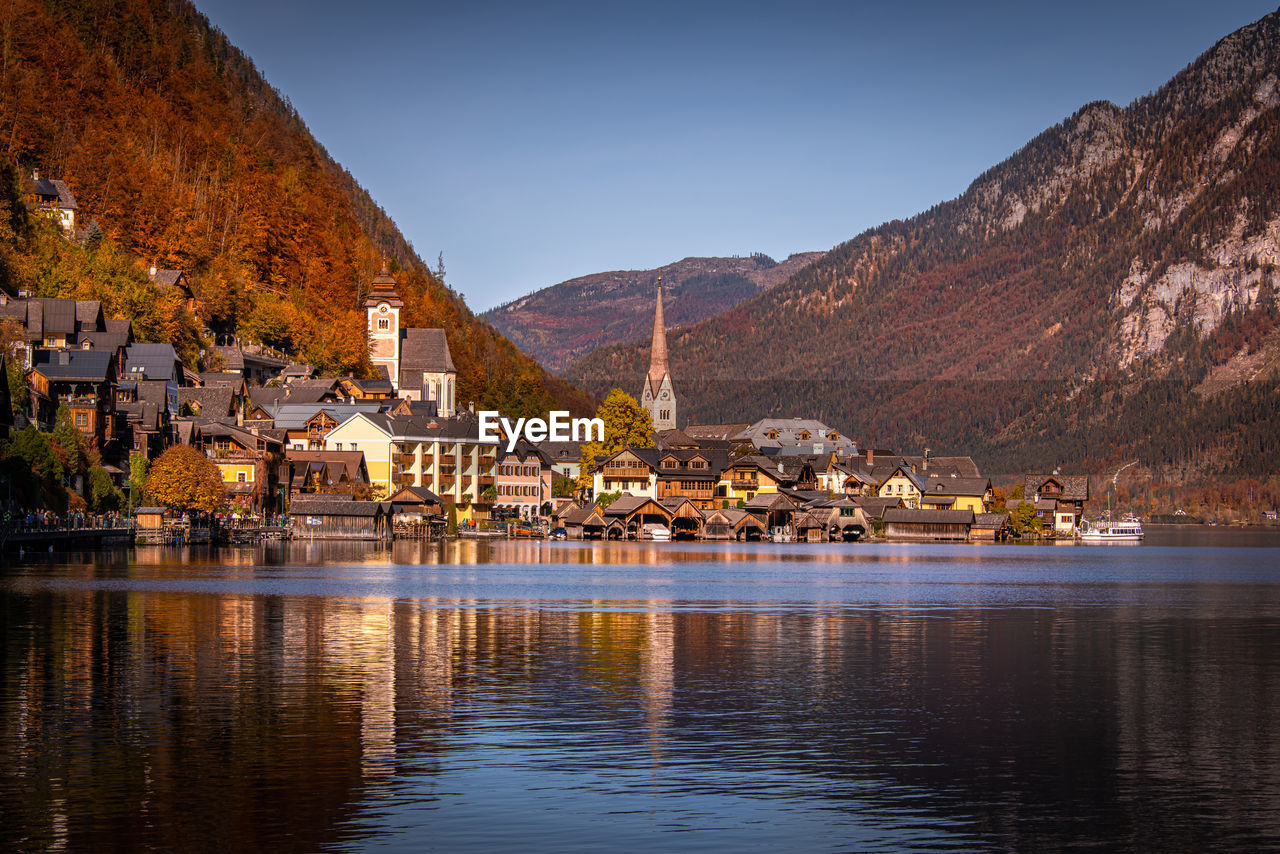 Houses by lake and buildings against sky in city - hallstatt