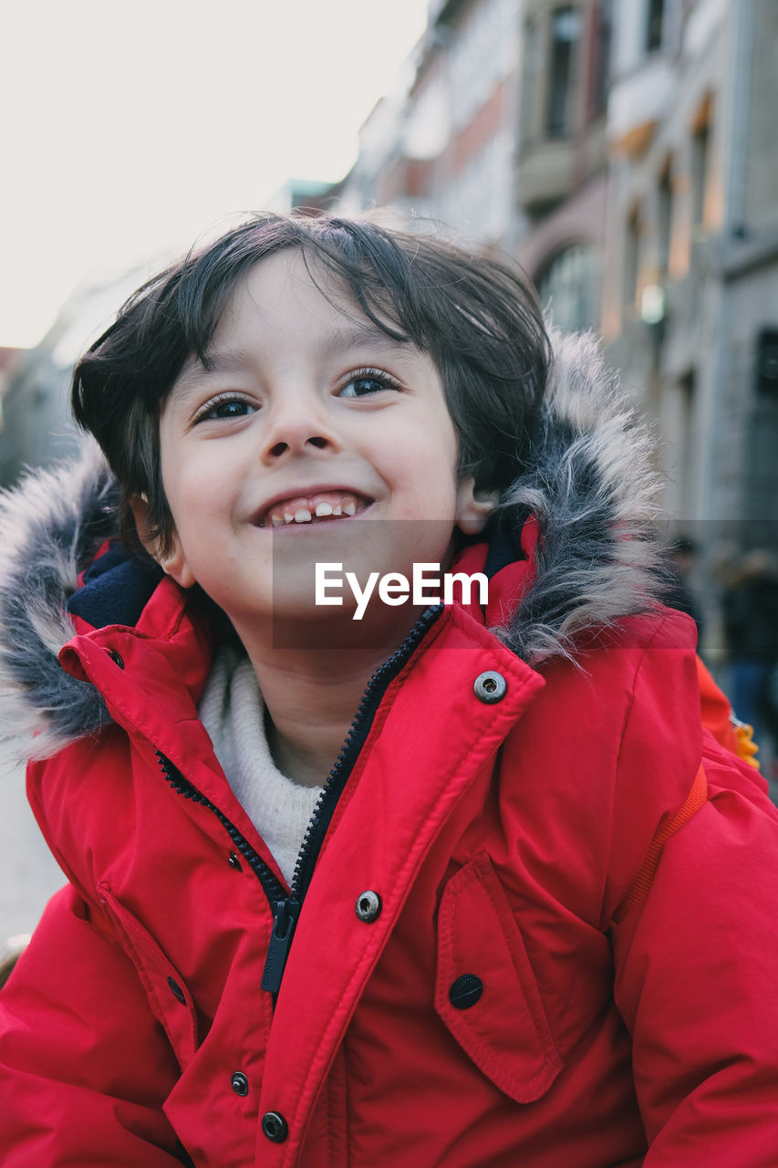 Portrait of cute 4 year old boy wearing red jacket looking away and smiling