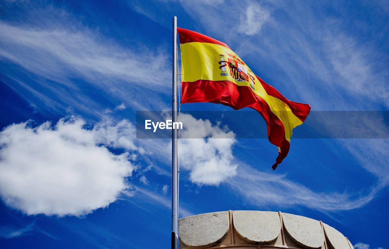 Low angle view of spanish flag waving against sky