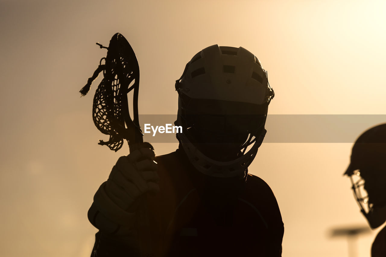 Silhouette lacrosse players against sky during sunset