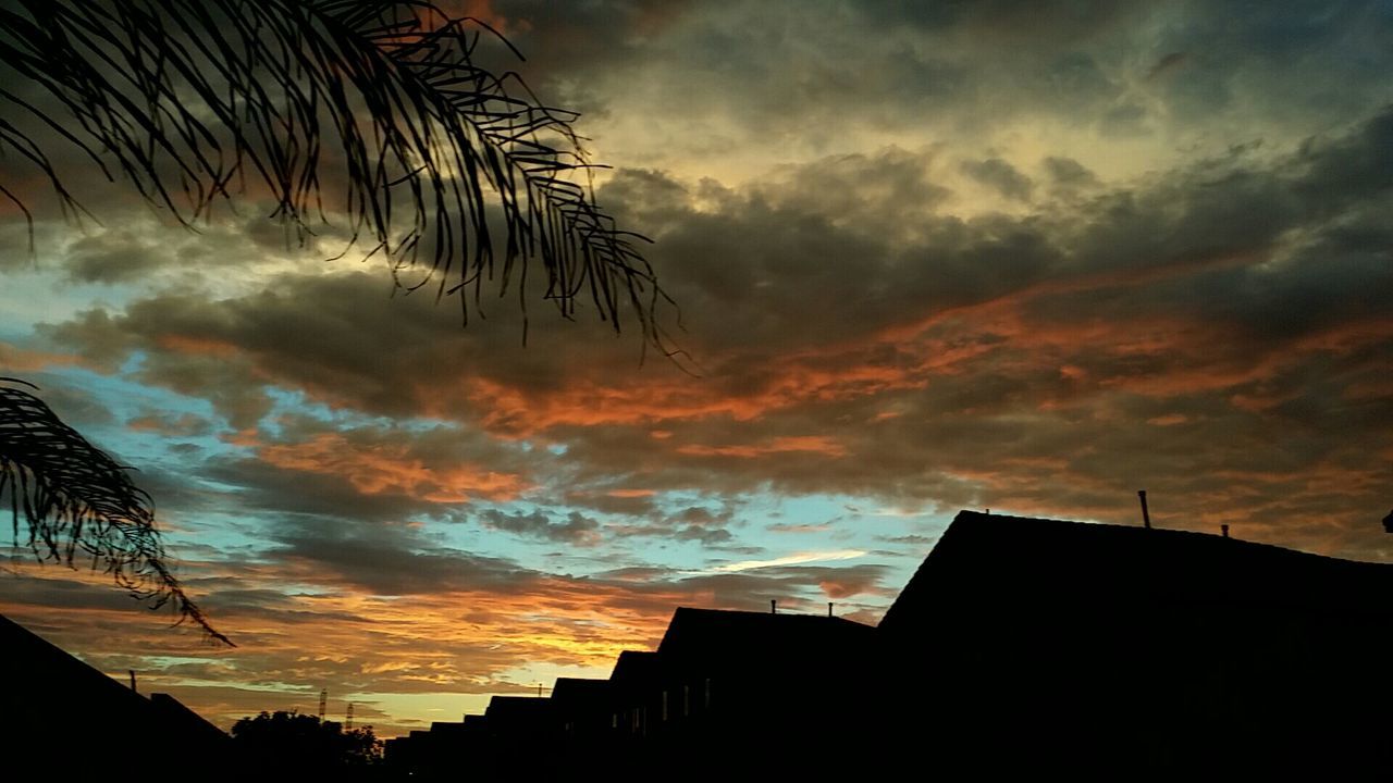 Low angle view of silhouette buildings against cloudy sky during sunset