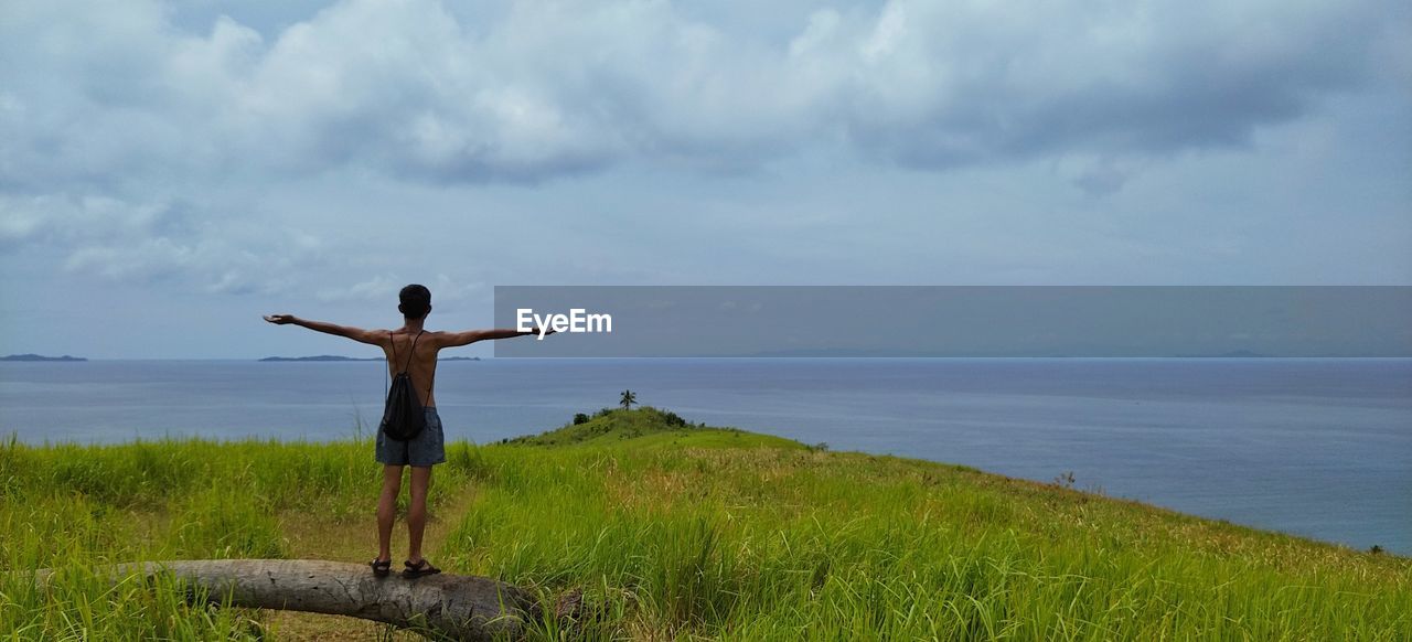 Rear view of man standing on rock by sea against sky