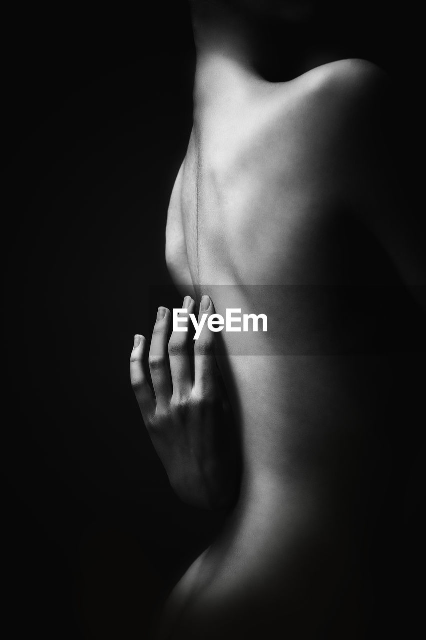 Midsection of shirtless woman against black background