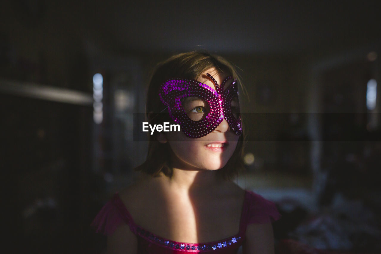 Close-up of small child lit up in dark room wearing butterfly costume