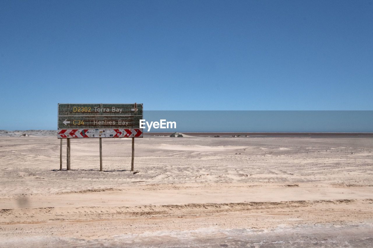 Information sign on beach against clear blue sky