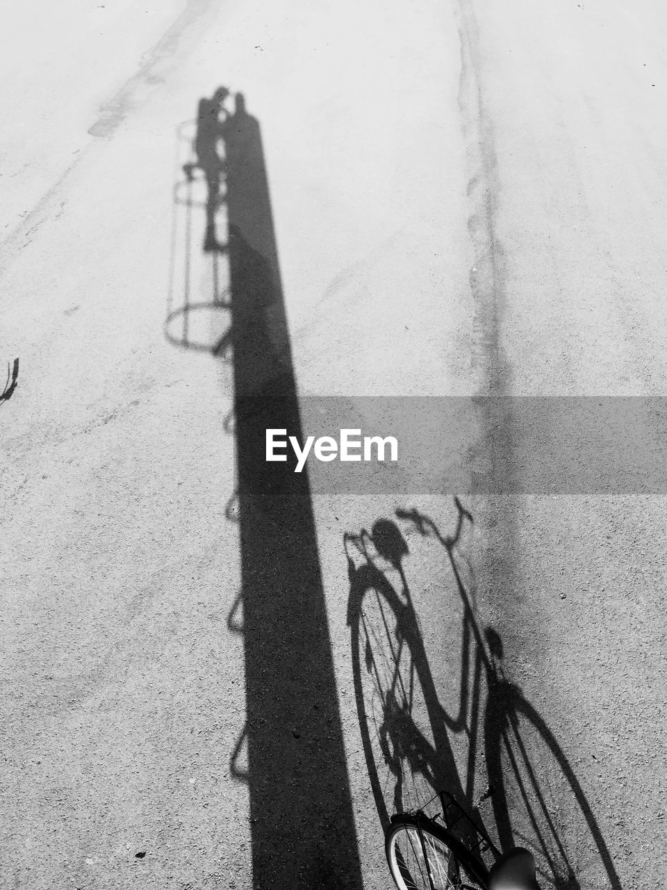 Shadow of bicycle parked by pole on street