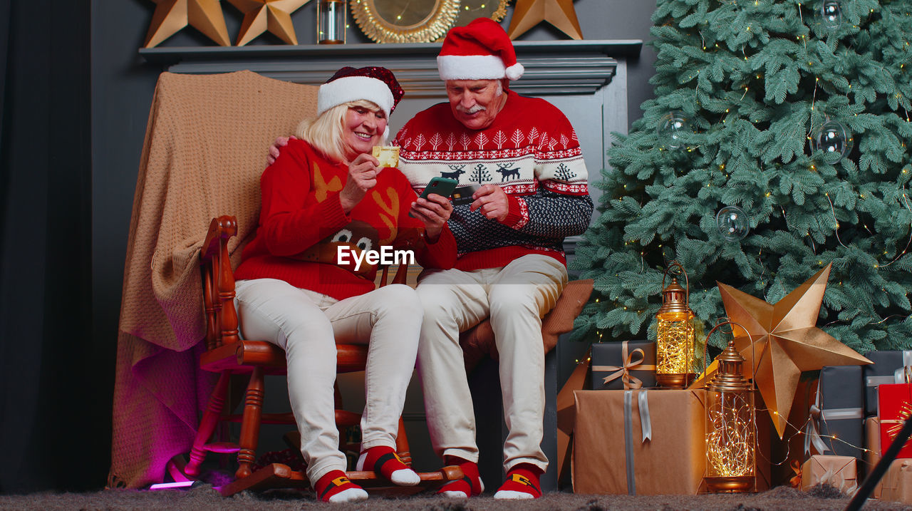 Senior couple sitting on chair while shopping online during christmas