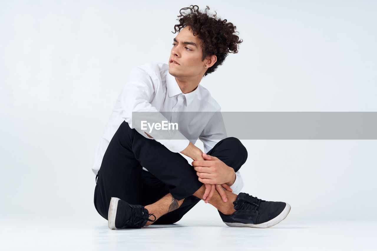 YOUNG MAN SITTING AGAINST WHITE BACKGROUND