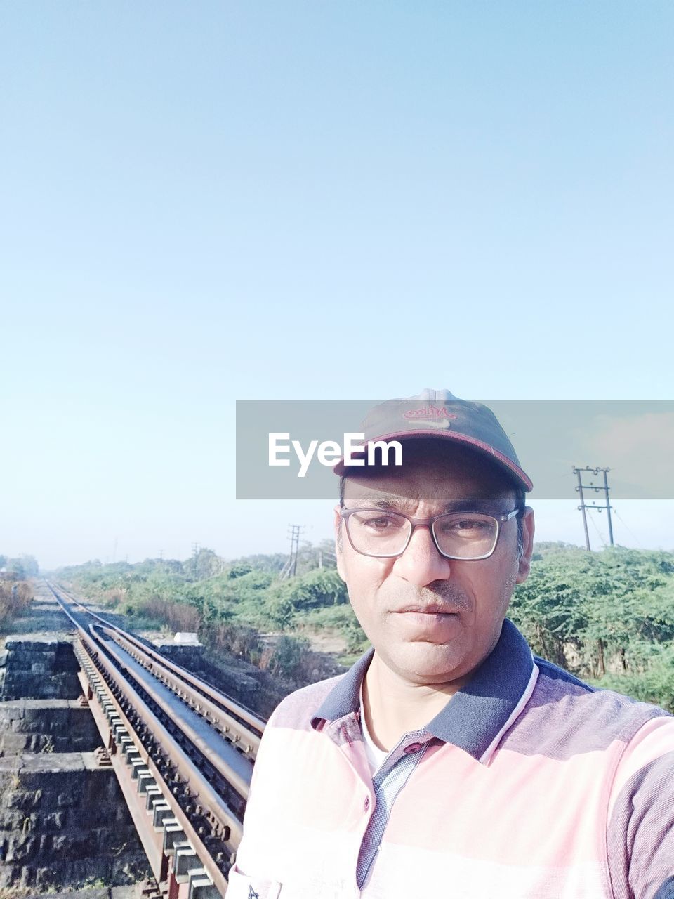 PORTRAIT OF YOUNG MAN AGAINST RAILROAD TRACK AGAINST SKY