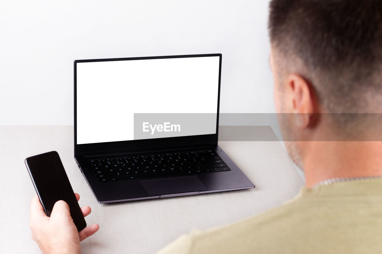 REAR VIEW OF MAN USING SMART PHONE ON TABLE