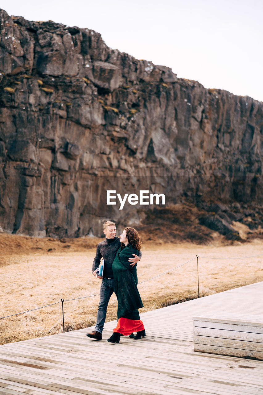 REAR VIEW OF COUPLE STANDING ON ROCK